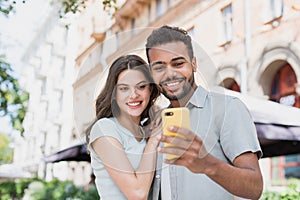 Young couple using smartphone outdoors. Joyful smiling woman and man looking at mobile phone in a city