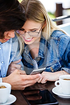 Young couple using smartphone while sitting together in cafe