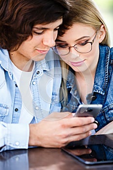 Young couple using smartphone while sitting together in cafe