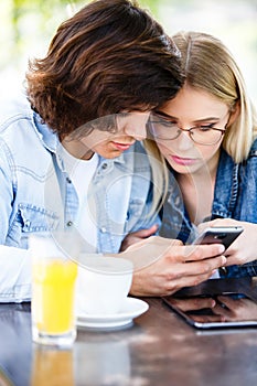 Young couple using smartphone while sitting together in cafe