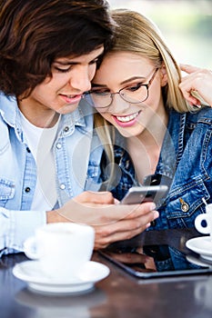 Young couple using smartphone while sitting together in cafe