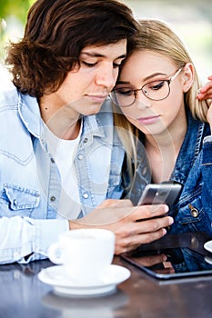 Young couple using smartphone while sitting together in cafe