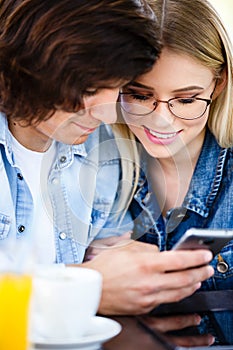 Young couple using smartphone while sitting together in cafe