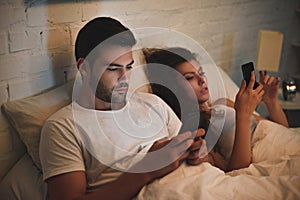 young couple using smartphones while lying in bed