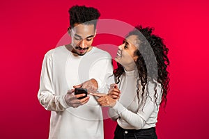 Young couple using their mobile devices, laughing and talking about it. Social apps on red studio background