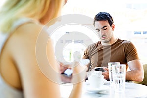 Young couple using their mobile phones while sitting at cafe