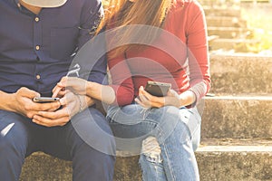 Young couple using their smartphones are sitting in a park, which conveys the concepts of technology social media
