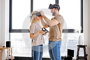 Young couple using virtual reality simulator playing games in living room, copy space