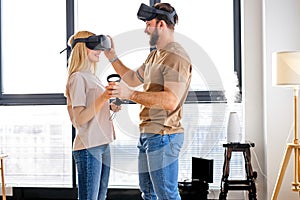 Young couple using virtual reality simulator playing games in living room, copy space