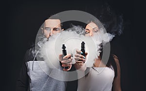 Young couple vaping e-cigarette with smoke on black closeup