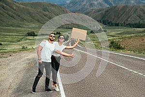 A young couple is voting on the road. A happy couple hitchhiking and voting with a sign on the road. Happy man and woman