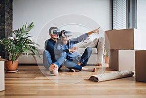 A young couple with VR goggles sitting on a floor, moving in a new home.