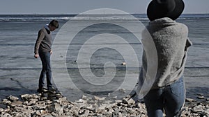 Young couple walk on a rocky shore near a rock near a river covered with ice