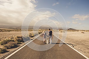 Young couple walk together on a long straight road in the middle of a desert nowhere place - life and love and relationship