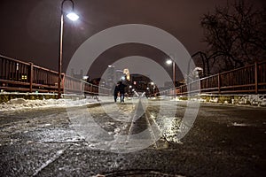 Young couple walking across a river bridge in the city at night in winter