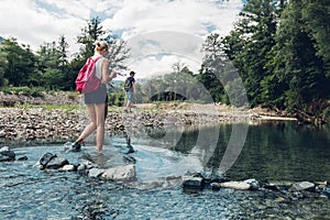 Young Couple Walking Along The Coast Of Mountain River In Summer. Girl Wading Across The River