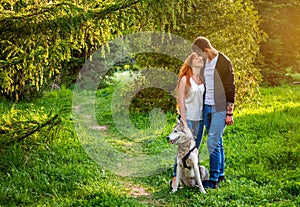 A young couple walking a dog in the park