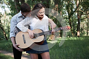 Young couple walking in the forest, playing guitar and dancing, summer nature, bright sunlight, shadows and green leaves, romantic