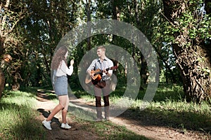 Young couple walking in the forest, playing guitar and dancing, summer nature, bright sunlight, shadows and green leaves, romantic