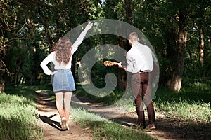 Young couple walking in the forest, playing guitar and dancing, summer nature, bright sunlight, shadows and green leaves, romantic