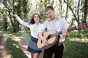 Young couple walking in the forest, playing guitar and dancing, summer nature, bright sunlight, shadows and green leaves, romantic