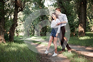 Young couple walking in the forest, playing guitar and dancing, summer nature, bright sunlight, shadows and green leaves, romantic