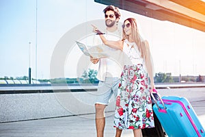 Young couple walking in front of an airport terminal building, pulling suitcases