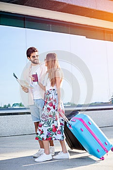 Young couple walking in front of an airport terminal building, pulling suitcases