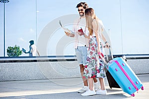 Young couple walking in front of an airport terminal building, pulling suitcases