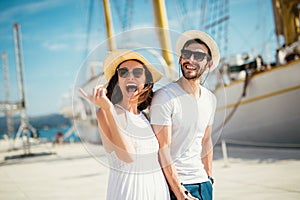 Young couple walking by the harbor of a touristic sea resort with sailboats on background