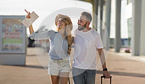 Young couple walking out airport with baggage, copy space
