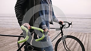 Young couple walking by seaside on bikes in autumn cloudy day. Footage of rudders with hands. People, activity, leisure