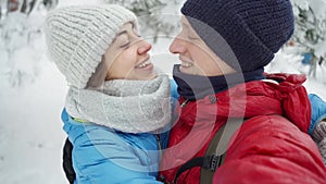 Young couple walking in snowy winter park at cold winter day. man and woman lovely hugging kissing and laughing.