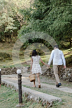 Young couple is walking together up a grassy hill, holding hands and smiling