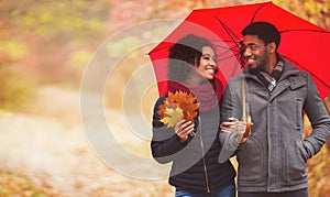 Young couple walking under umbrella at rainy autumn day