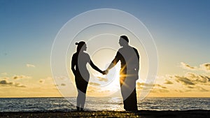Young couple is walking in the water on summer beach. Sunset over the sea.Two silhouettes against the sun. Just married