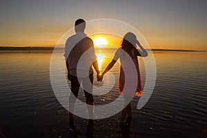 Young couple is walking in the water on summer beach. Sunset over the sea.Two silhouettes against the sun. Just married couple