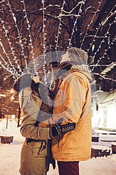 Young couple walking in winter city center under holiday illumination