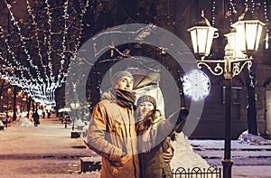 Young couple walking in winter city center under holiday illumination