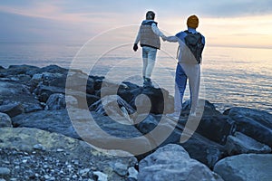 A young couple walks along the seashore at sunset. A man and a woman in casual clothes standing backs
