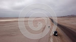 Young couple walks on highway, car at roadside parked in desert. White SUV.