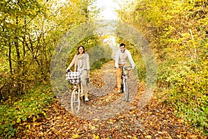 Young couple in warm clothes cycling in autumn park.