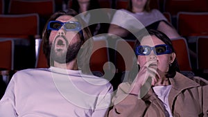 Young couple watching horror movie in 3D glasses. Media. Man and woman looking frightened and shocked while watching