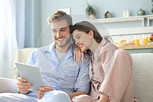 Young couple watching media content online in a tablet sitting on a sofa in the living room