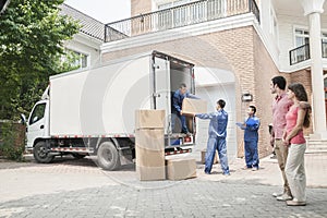 Young couple watching movers move boxes from the moving van