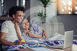 Young couple watching a movie on their laptop in bed