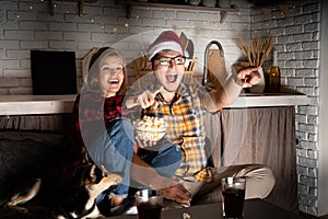 Young couple watching movies at home at christmas pointing to the screen