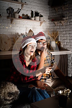 Young couple watching movies at home at christmas pointing to the screen