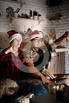 Young couple watching movies at home at christmas pointing to the screen