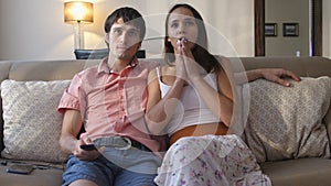 Young couple watching scary movie on TV with scared faces